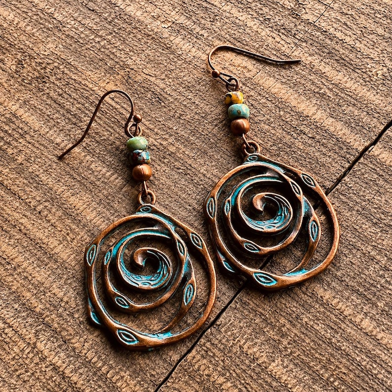 May include: Copper-coloured spiral earrings with turquoise accents and small beads. The earrings have a unique, artistic design with a rustic, bohemian aesthetic. The spiral design is accented with small leaf shapes.