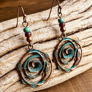 May include: A pair of copper-toned earrings featuring a spiral design with turquoise and red beads. The earrings have a hook fastening and a distressed finish, ideal for a bohemian or nature-inspired style.