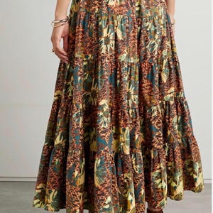 May include: A tiered maxi skirt featuring an elasticated waistband and a multi-coloured print. The fabric displays a repeating pattern of dark brown, olive green, and yellow floral motifs interspersed with a textured, animal-inspired print.