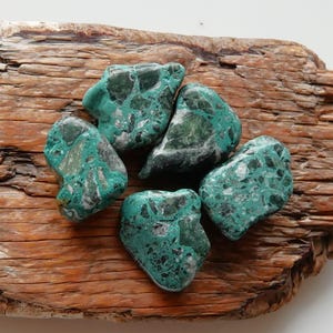 May include: Five tumbled green and white stones with a mottled pattern. The stones are on a piece of weathered wood.