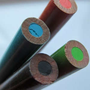 Op de afbeelding: Vier houten potloden met verschillende gekleurde stiften. De potloden zijn gestapeld, met het potlood met rode stift bovenaan, gevolgd door de potloden met blauwe, zwarte en groene stift.