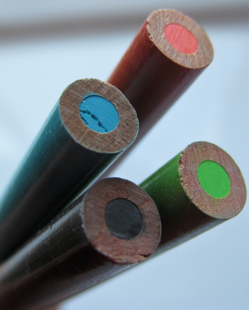 Op de afbeelding: Vier houten potloden met verschillende gekleurde stiften. De potloden zijn gestapeld, met het potlood met rode stift bovenaan, gevolgd door de potloden met blauwe, zwarte en groene stift.