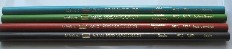 Op de afbeelding: Vier Prismacolor kleurpotloden met etiketten in het Spaans en Engels. De potloden zijn gelabeld "Azul  Azuliano PC 905", "Verde Primavera PC 913", "Bermellon Brillo PC 921", en "Sepia PC 942".