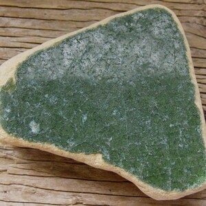 Peut inclure: Une pièce de poterie triangulaire avec un glaçage vert et un bord blanc. Le glaçage a un effet craquelé.