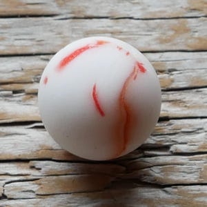May include: White marble sphere with red and orange marbling.