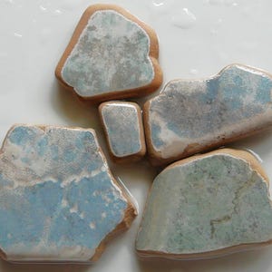 May include: Five irregularly shaped ceramic tiles with a light blue glaze and brown edges. The glaze has a mottled appearance with areas of white and light blue.