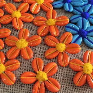 May include: A close-up of orange and blue fabric flowers with yellow and blue centers. The flowers are arranged on a burlap background.