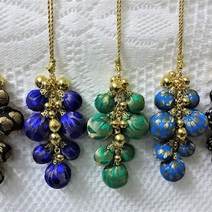 May include: Five fabric tassels with gold beads and chains. The tassels are in black with gold accents, blue with gold accents, green with gold accents, blue with gold accents, and black with white polka dots.
