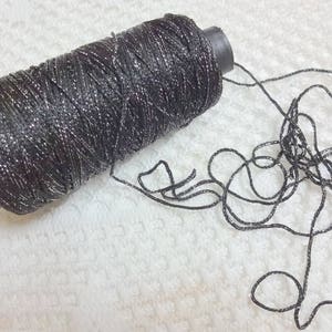 Puede incluir: Una bobina de hilo plateado y negro con un extremo de hilo suelto.