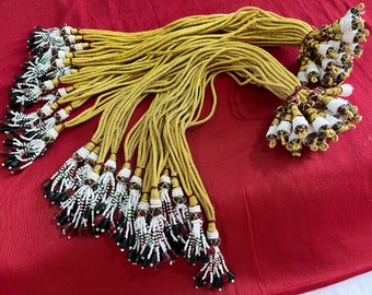 May include: A group of gold cords with beaded tassels. The tassels are made with white, red, and green beads.