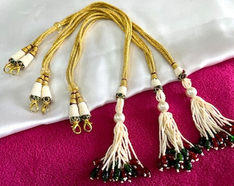 May include: Three gold cords with white and green beaded tassels. The tassels have red and green accents.