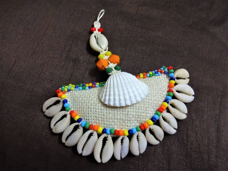 May include: A handmade wall hanging with a white seashell, colorful beads, and a burlap background. The seashells are arranged in a semi-circle shape.