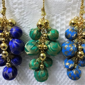 May include: Three fabric tassels with gold beads and a gold chain. The tassels are blue, green, and blue with gold accents.