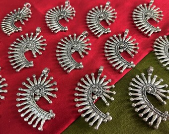 May include: A collection of silver-toned metal pendants in the shape of a spiral with a decorative design. The pendants are arranged on a red and green fabric background.