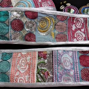 Peut inclure: Deux bandes de galon en tissu avec une bordure argentée. Le galon est composé de tissus de différentes couleurs avec des motifs brodés, notamment des cercles, des volutes et des motifs floraux. Le galon est décoré de paillettes et de perles.
