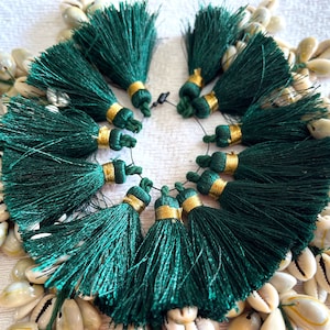 May include: A set of 12 green tassels with gold trim. The tassels are arranged in a circle and are surrounded by white seashells.