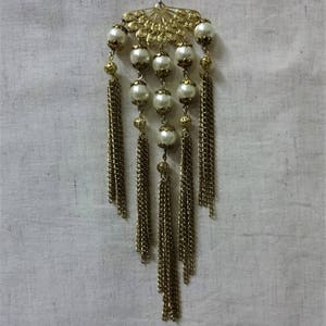 K&ouml;nnte beinhalten: Ein goldfarbener Haarkamm mit einem f&auml;cherf&ouml;rmigen Design und Perlen. Der Kamm hat mehrere goldene Ketten mit Quasten.