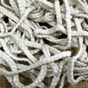 May include: A close-up of a pile of white braided rope. The rope is made of a soft, natural fibre and has a smooth, even texture.