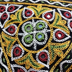 May include: Close-up of a black fabric with intricate embroidery in white, gold, and green thread. The embroidery features a circular design with small mirrors sewn into the fabric.