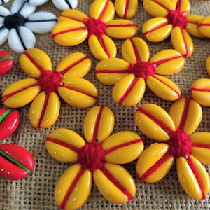 May include: A collection of yellow flower-shaped buttons with red centers and red stripes. The buttons are made of a smooth, shiny material and have a slightly raised center.