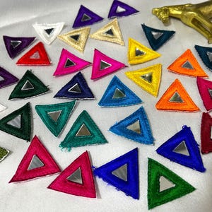 May include: A collection of small, triangular fabric patches in various colors including red, blue, green, yellow, orange, purple, and white. Each patch features a central triangular mirror insert. A small, gold-colored horse figurine is visible.