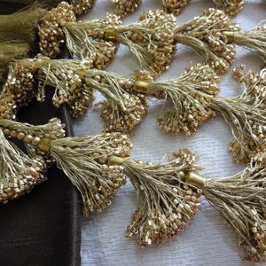 May include: A group of gold tassel trims with a beaded detail. The tassels are made of a fine, light brown thread and have a delicate, elegant look.