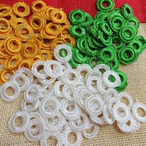 Op de afbeelding: Een verzameling gehaakte ringen in drie kleuren: geel, groen en wit. De ringen zijn in een halve cirkel op een jute achtergrond gerangschikt.