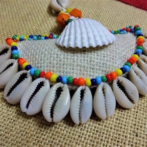 May include: A colorful beaded necklace with a white seashell pendant and cowrie shells hanging from the bottom.