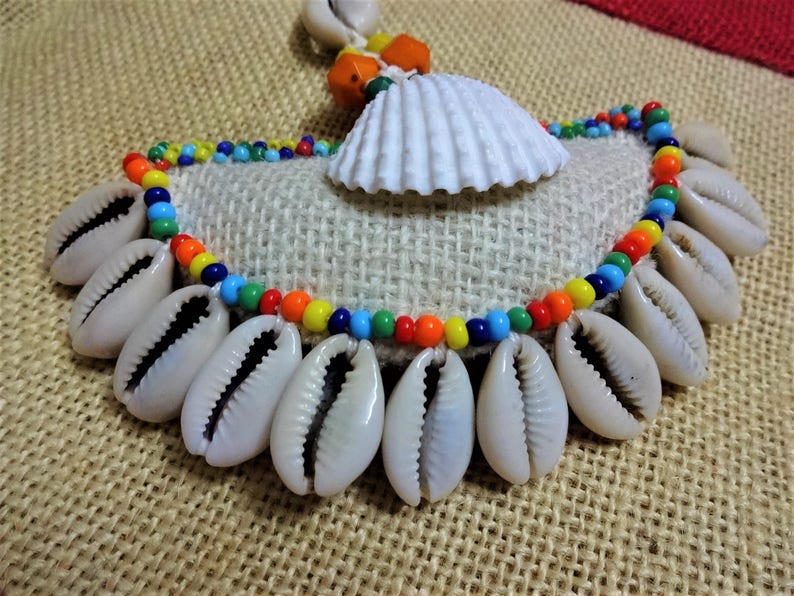 May include: A colorful beaded necklace with a white seashell pendant and cowrie shells hanging from the bottom.