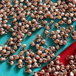 May include: A large group of small, round, copper-colored metal charms with a loop on top. The charms are scattered on a blue and red surface.