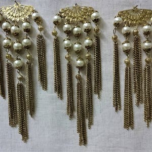 K&ouml;nnte beinhalten: Drei goldfarbene Ohrringe mit Perlenakzenten und baumelnden Ketten. Jeder Ohrring hat ein dekoratives F&auml;cherdesign mit einem filigranen Muster.
