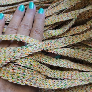 Könnte beinhalten: Nahaufnahme eines Bündels geflochtener Jutekordel mit durchgängig eingewebten bunten Fäden. Die Kordel ist in natürlicher beige Farbe mit Akzenten in Grün, Gelb, Orange und Rot.