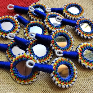Può includere: Un gruppo di piccoli specchi rotondi fatti a mano con ricami in filo blu, bianco, giallo e rosso. Gli specchi sono attaccati a manici in filo blu.
