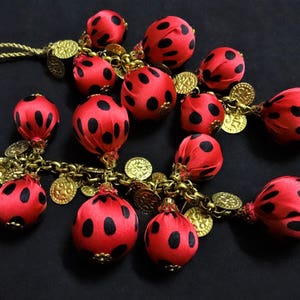 May include: A red and black polka dot garland with gold accents. The garland is made of fabric and has a chain link design.