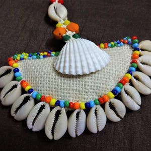 May include: A colorful beaded necklace with a white seashell pendant and a burlap backing. The beads are in shades of red, orange, yellow, green, blue, and purple.