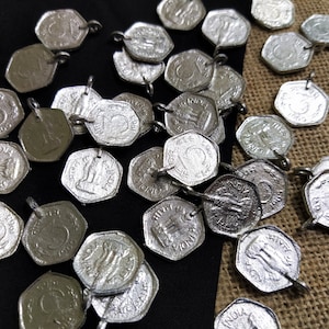 Puede incluir: Una colección de dijes de metal de color plateado con forma de monedas con el texto "FIVE RUPEES INDIA" en ellos. Los dijes tienen un agujero en la parte superior para sujetarlos a un collar o pulsera.