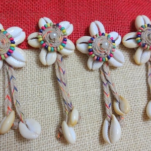 May include: Five white seashell flower ornaments with colorful beads and a white pearl in the center. Each ornament has a long, braided cord with white seashells hanging from it.