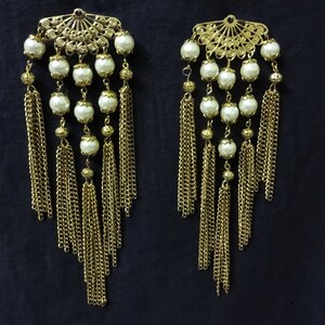 K&ouml;nnte beinhalten: Ein Paar goldfarbene Ohrringe mit wei&szlig;en Perlenakzenten und baumelnden Ketten.