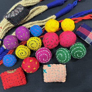 Könnte beinhalten: Eine Sammlung von bunten, handgefertigten Stoffkugeln und Quadraten mit verschiedenen Stickereien. Die Kugeln sind in den Farben Rosa, Rot, Gelb, Grün, Blau und Lila. Die Quadrate sind in den Farben Rosa, Rot und Blau.