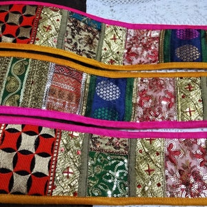 Può includere: Due strisce di passamaneria in tessuto colorato con bordi rosa e gialli. Il tessuto è fatto di un patchwork di diversi materiali, tra cui velluto, paillettes e ricami.