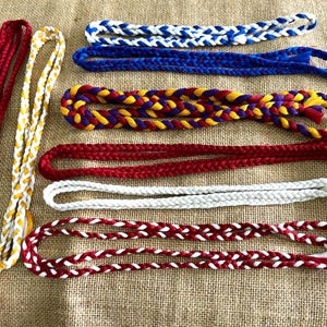 Puede incluir: Ocho cordones trenzados en varios colores, incluyendo rojo, blanco, azul, amarillo y morado. Los cordones están todos trenzados en un patrón similar y tienen un borla al final.