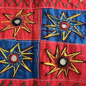 May include: A red and blue fabric patchwork with yellow and red embroidered stars. Each star has a circle in the centre.