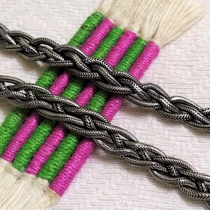 May include: Two silver braided chains on a white and green striped fabric background.