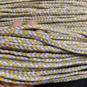 Peut inclure: Gros plan sur un cordon tressé avec des brins gris et jaunes alternés. Le cordon est doux et flexible, et il est parfait pour les projets de bricolage.