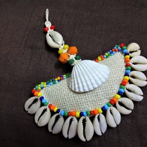 May include: A white seashell with a burlap background, surrounded by a colorful beaded trim and smaller white seashells.