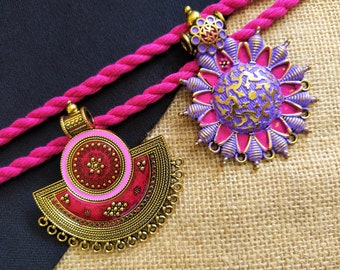 Puede incluir: Dos colgantes de oro adornados con esmalte rosa y morado. Los colgantes presentan diseños intrincados y son perfectos para agregar un toque de elegancia a cualquier atuendo.