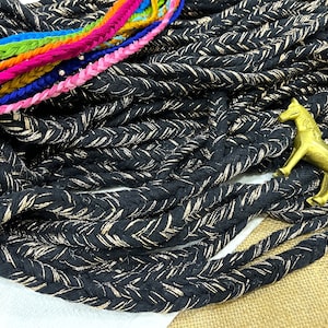 Pode incluir: Corda trançada preta com fio dourado tecido por todo o comprimento. A corda está empilhada em um monte com uma pequena figura de cavalo dourada no topo.
