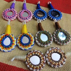 Peut inclure: Assortiment de miroirs ronds à main de différentes couleurs avec des bordures brodées. Chaque miroir a une couleur et un motif différents, notamment rose, bleu, jaune, vert et marron.