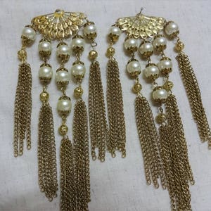 K&ouml;nnte beinhalten: Zwei goldfarbene Haarklammern mit Perlen und herabh&auml;ngenden goldenen Ketten. Die Klammern haben ein f&auml;cherf&ouml;rmiges Design.