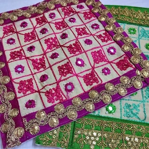 May include: Two square embroidered fabric coasters with gold trim. The top coaster is cream with pink embroidery and a pink border. The bottom coaster is cream with green embroidery and a green border.